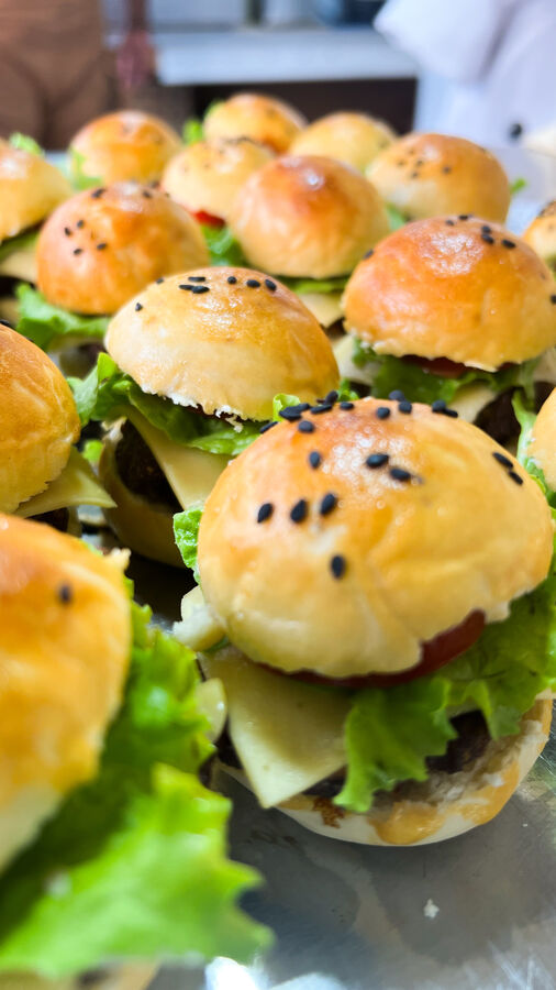 Mini hambúrgueres com gergelim preto, queijo e alface, prontos para venda no balcão