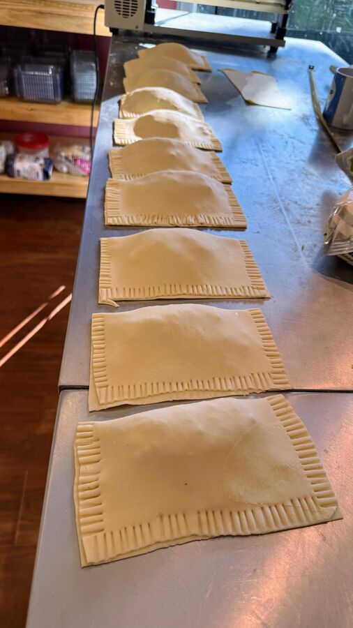 Pastéis de feira montados e selados com garfo, enfileirados na bancada