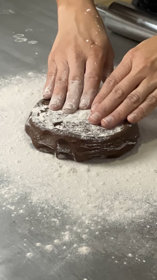 Mãos abrindo massa polvilhada de farinha sobre a bancada de inox